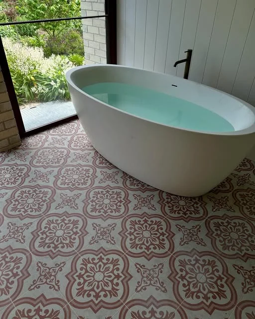 Freestanding bath on a patterned tiled floor with a garden view, tiled by Greyscale Tiling