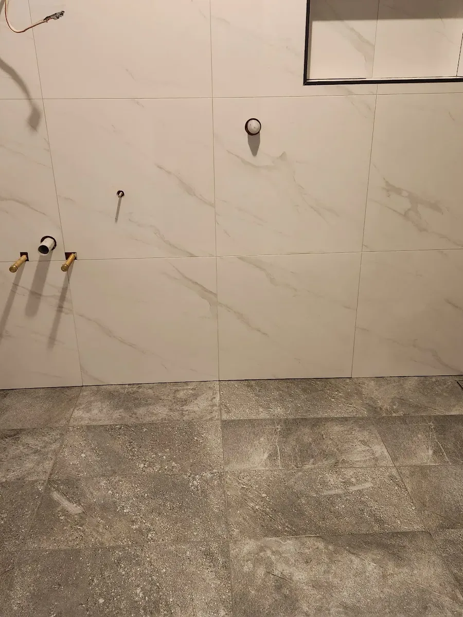 Walk in shower tiled by Howzat Tiling, marble look walls and a grey stone look floor with a strip drain