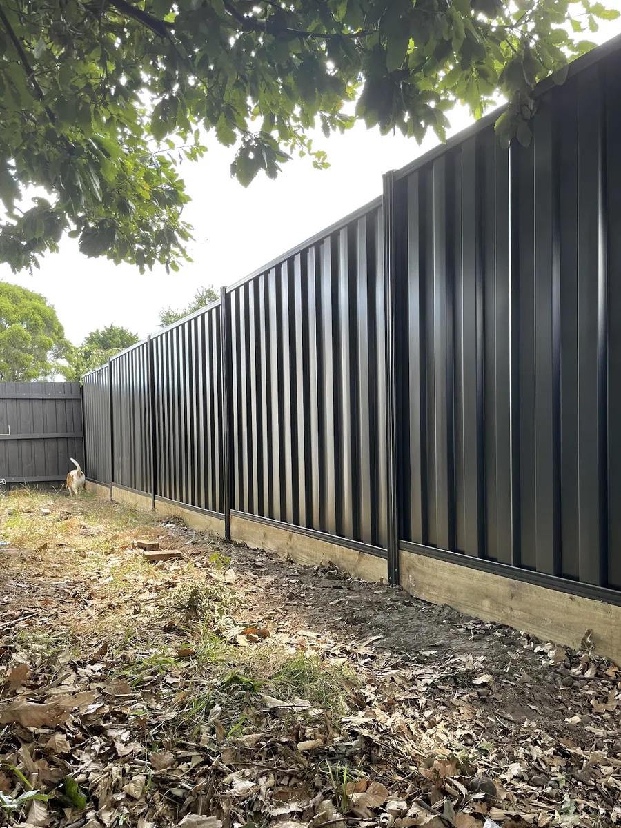A new dark Colorbond fence on steel posts with a timber plinth, built by JFK Fencing