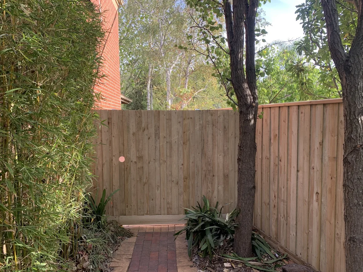 A new treated pine paling fence beside a brick house and bamboo, built by JFK Fencing