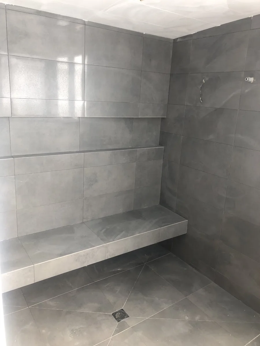 A large format grey tiled shower with a bench seat