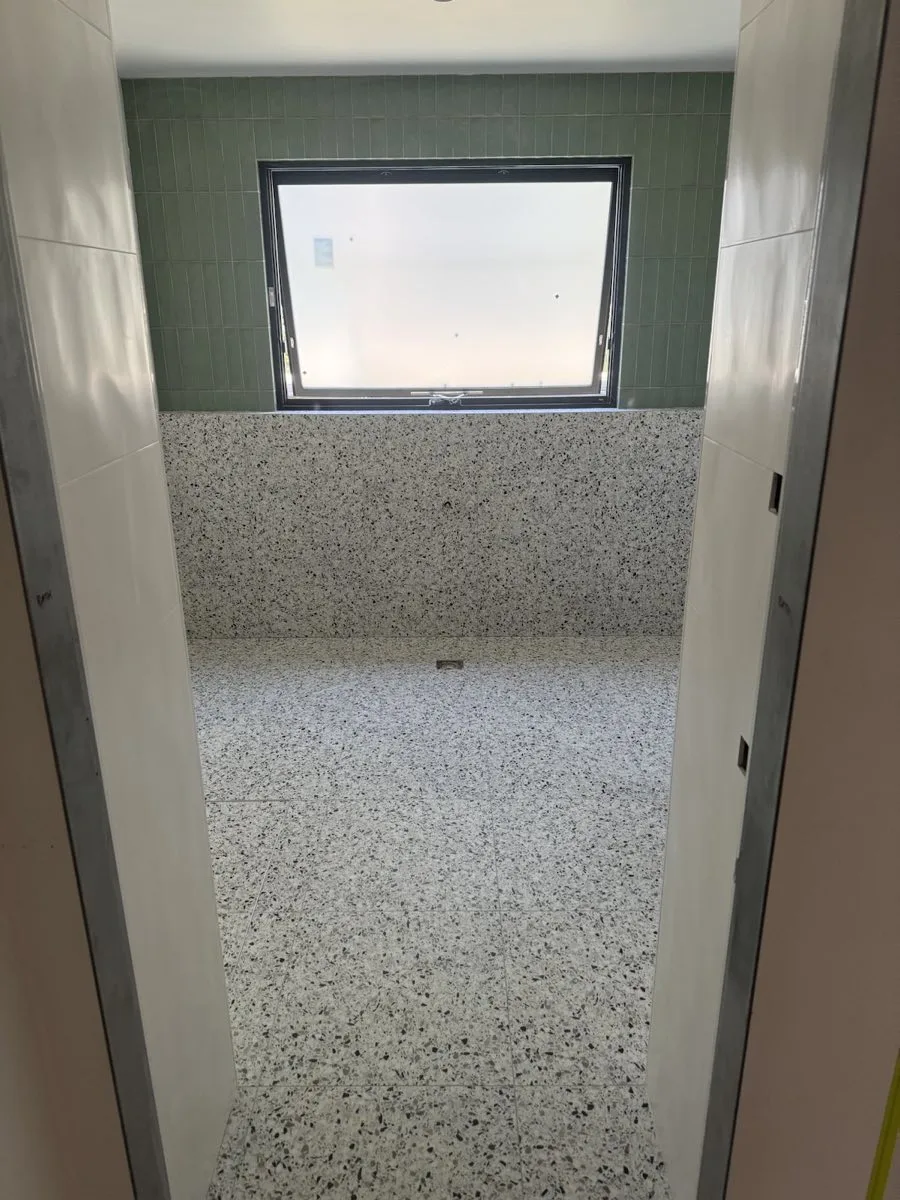 A terrazzo shower room with a green tiled wall and a window, tiled by MAK Tiling