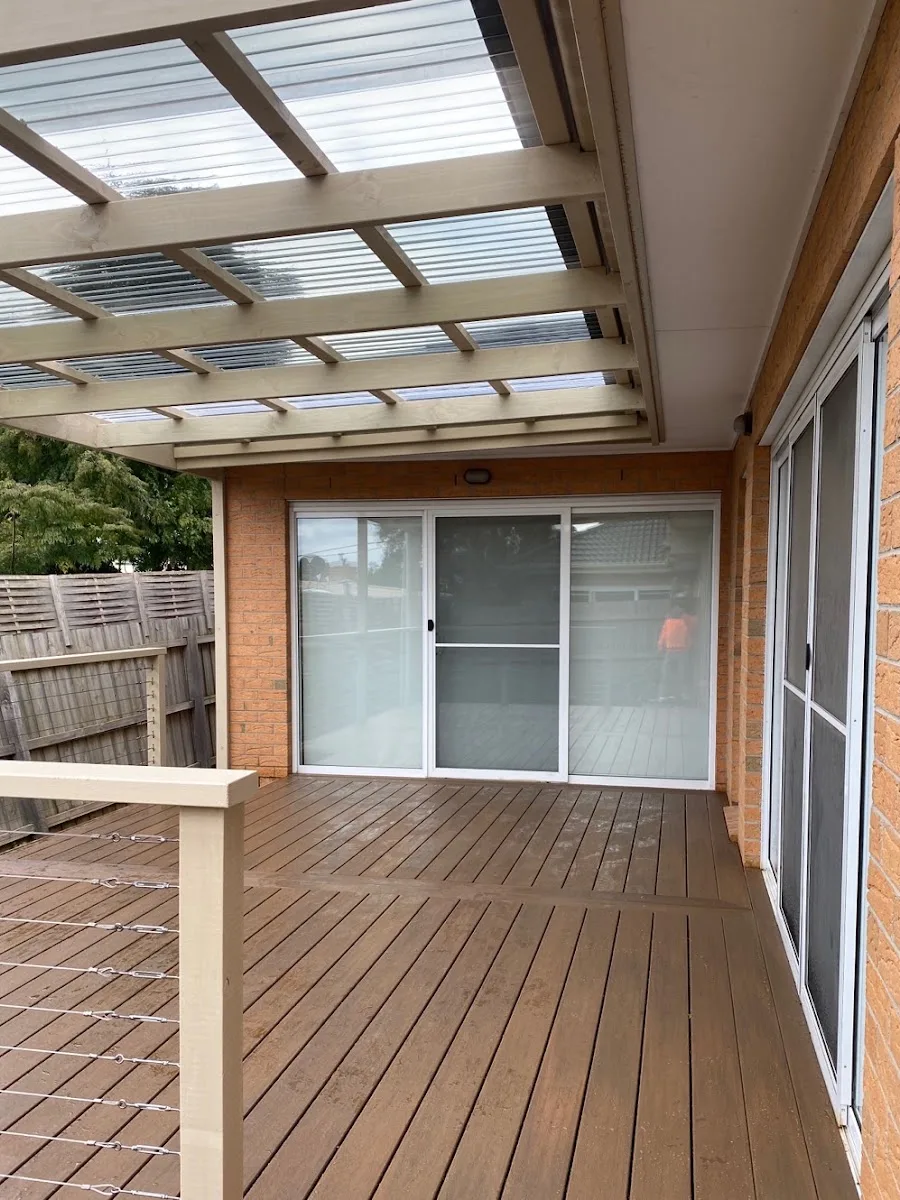 A new timber deck under a pergola with a clear roof, off the back of a brick home