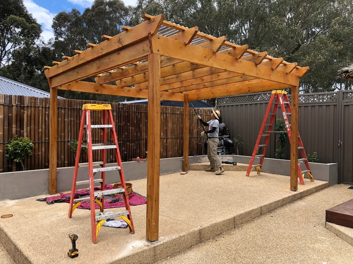 A timber pergola being oiled over a paved courtyard
