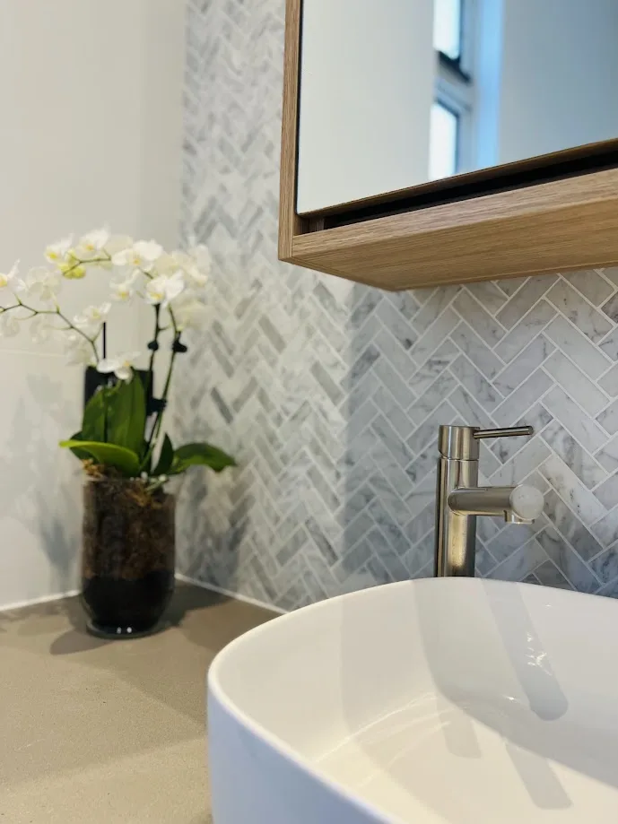 A herringbone marble feature wall behind a basin and an orchid