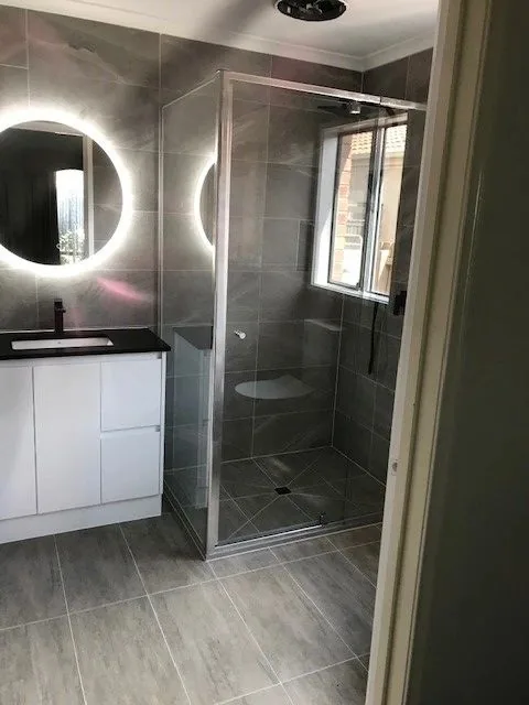 Renovated bathroom with a round LED mirror, grey stone look tiles and a frameless shower