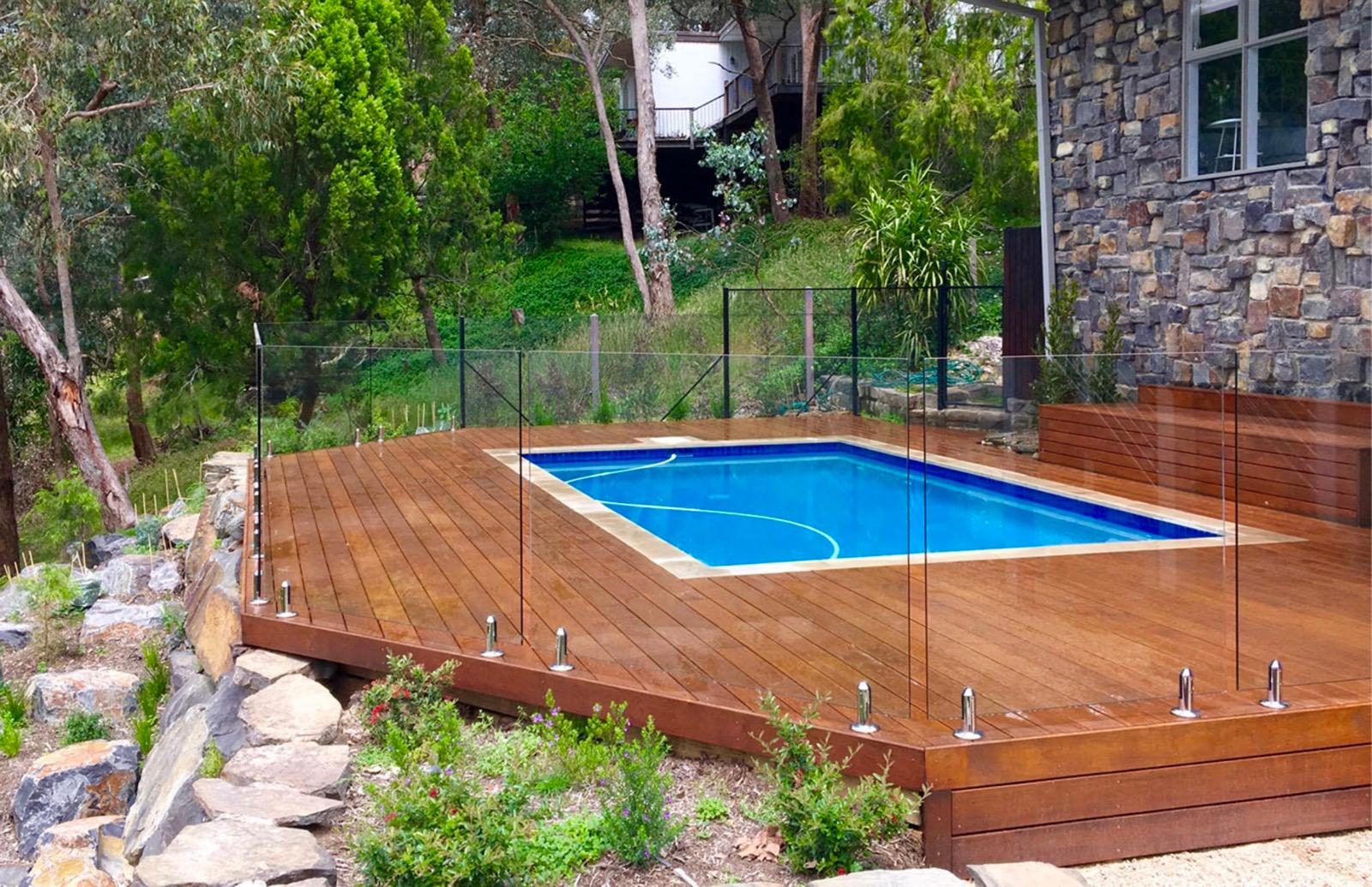 Timber pool deck with frameless glass fencing built around a backyard pool