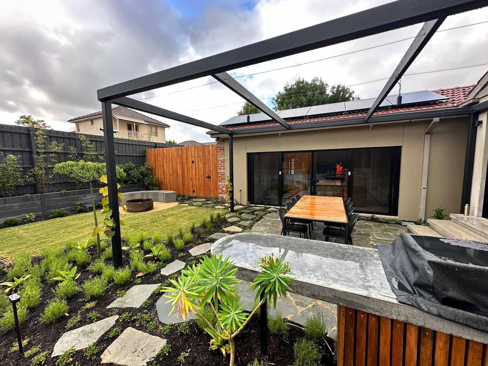 Completed backyard landscape with steel pergola, stepping-stone path, new planting and outdoor dining area