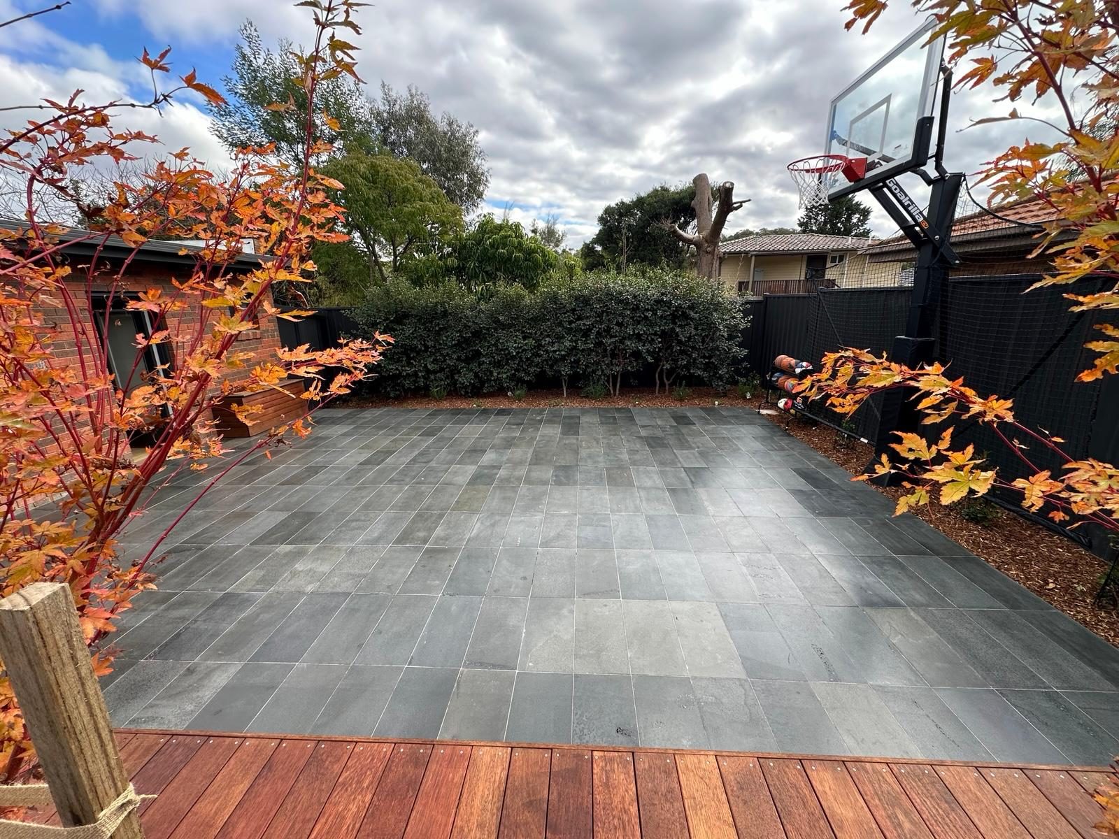 Slate-paved backyard court framed by a timber deck, hedge and Japanese maples