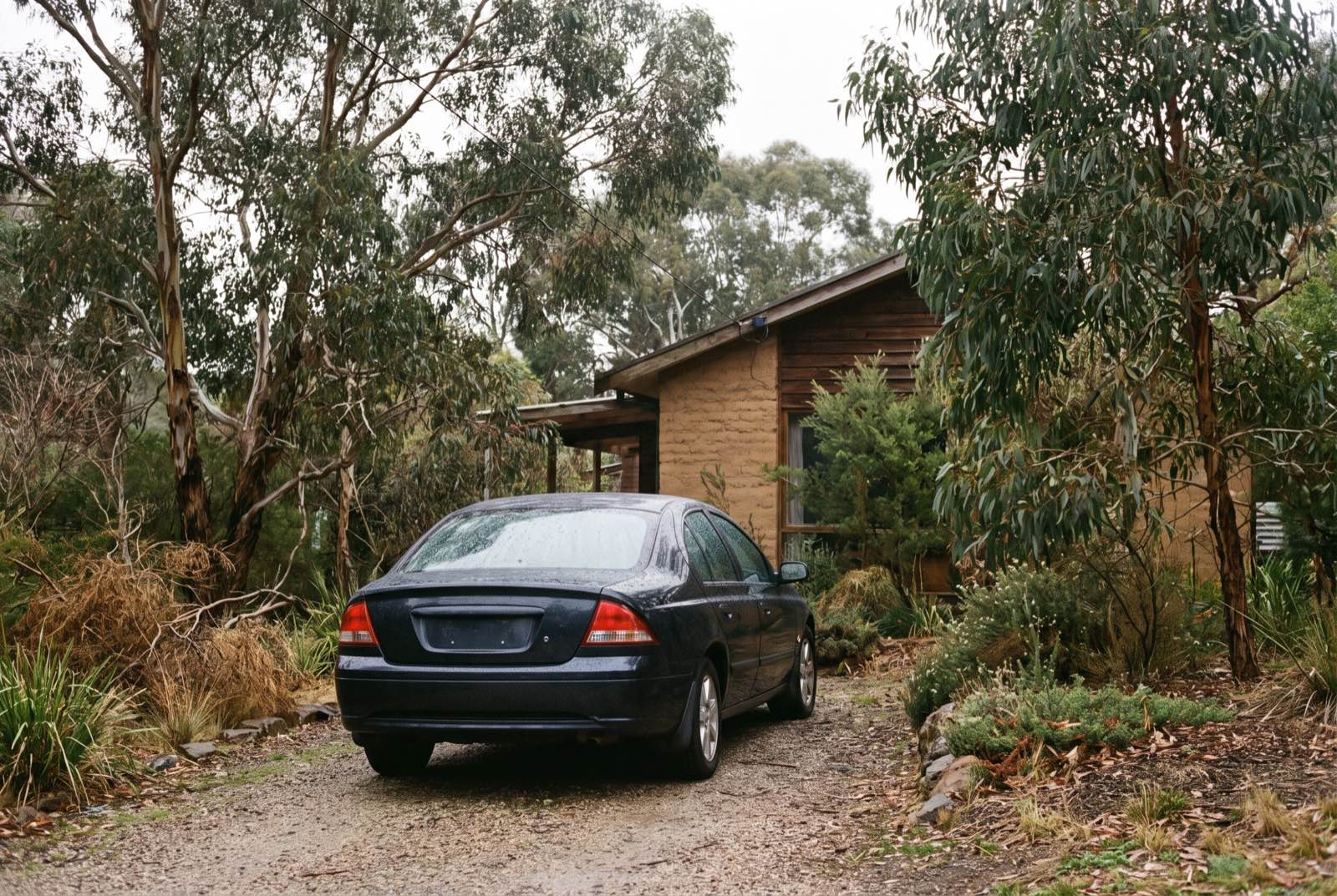 A freshly washed dark sedan in a leafy Eltham driveway beside a mudbrick house