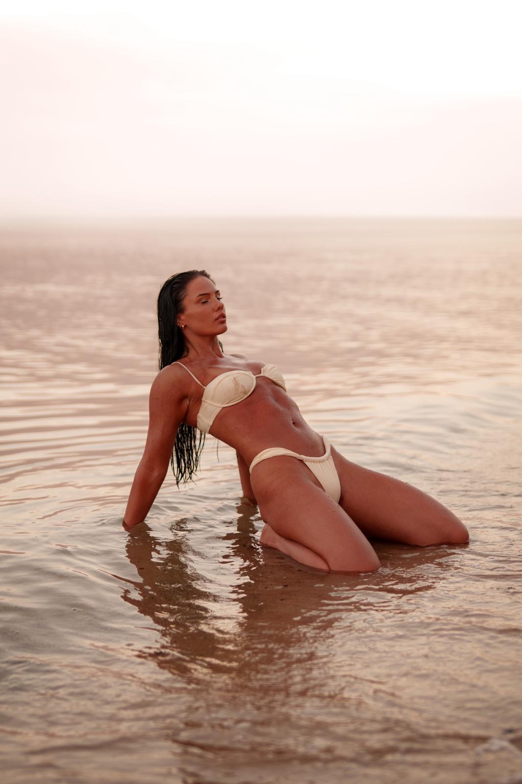 Woman kneeling in shallow ocean water at golden hour, warm cinematic light