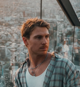 Jayden Sims, Melbourne photographer, in a plaid shirt with a city backdrop