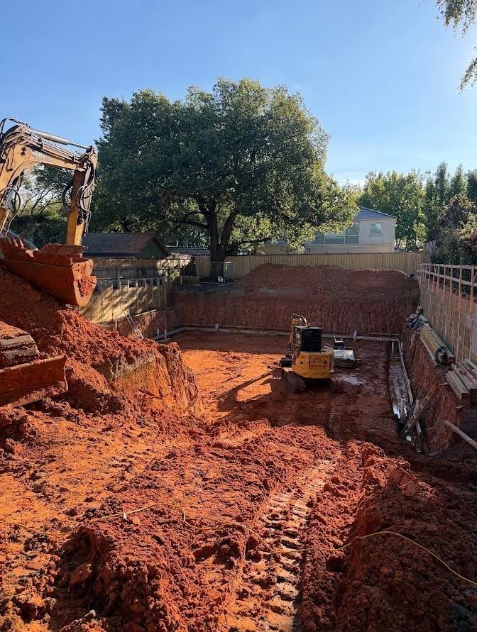 A deep cut through orange clay with a mature tree left in place rather than taken out.