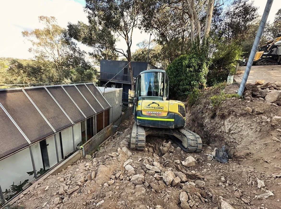 A machine working roughly a metre off the wall of a house, on rock, with the garden still standing.