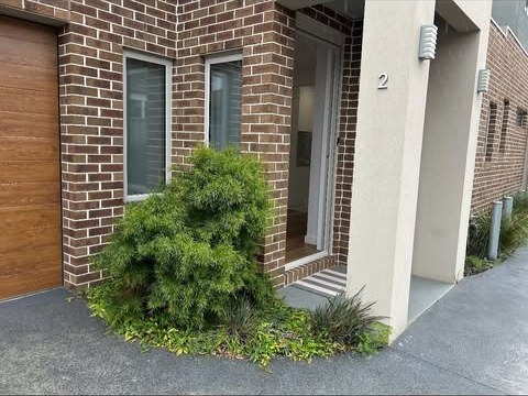 The front of a brick townhouse with a shaped shrub and swept entry