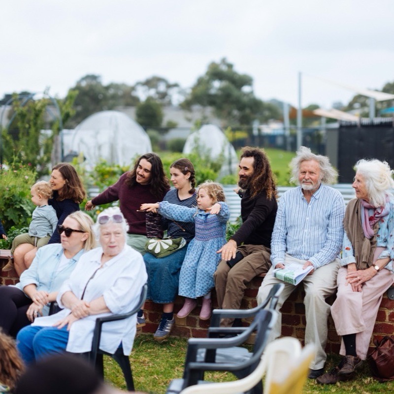 Families of every age sitting together on a garden wall watching the music