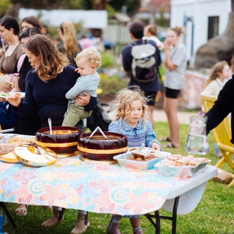 A parent holding a toddler beside a table laid with cakes and shared dishes