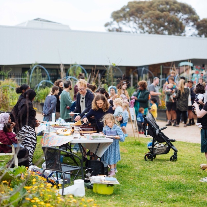 A long shared table of food with families serving each other on the lawn