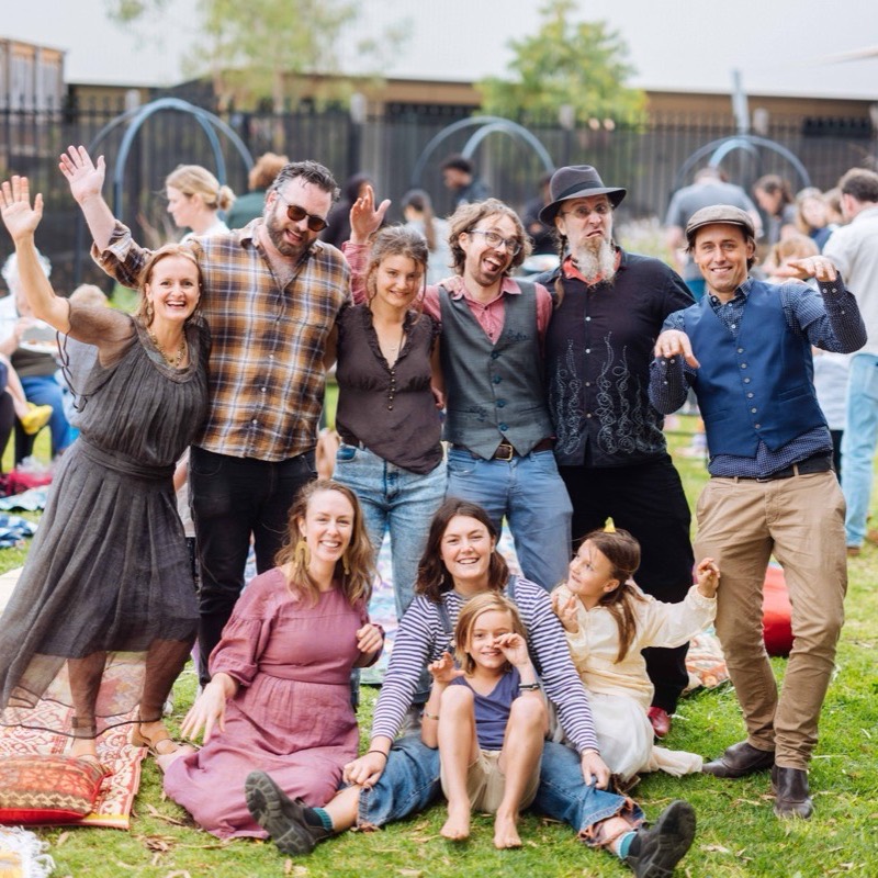 Parents, grandparents and children gathered on rugs on the grass, waving and laughing together