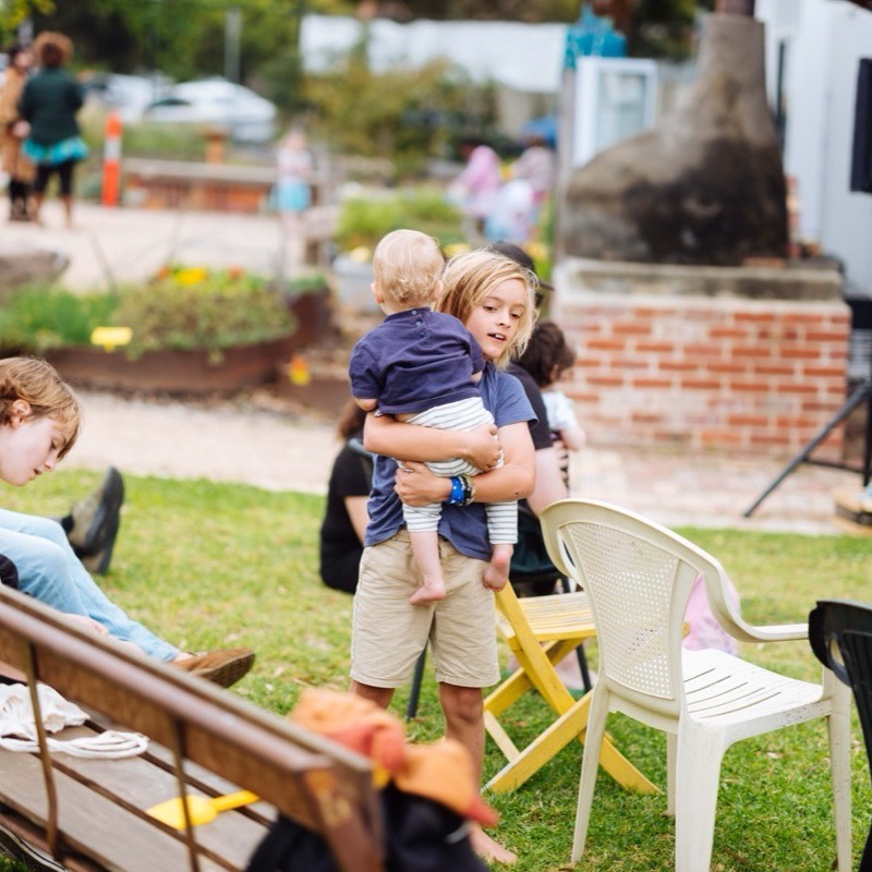 An older child carefully carrying a toddler across the grass