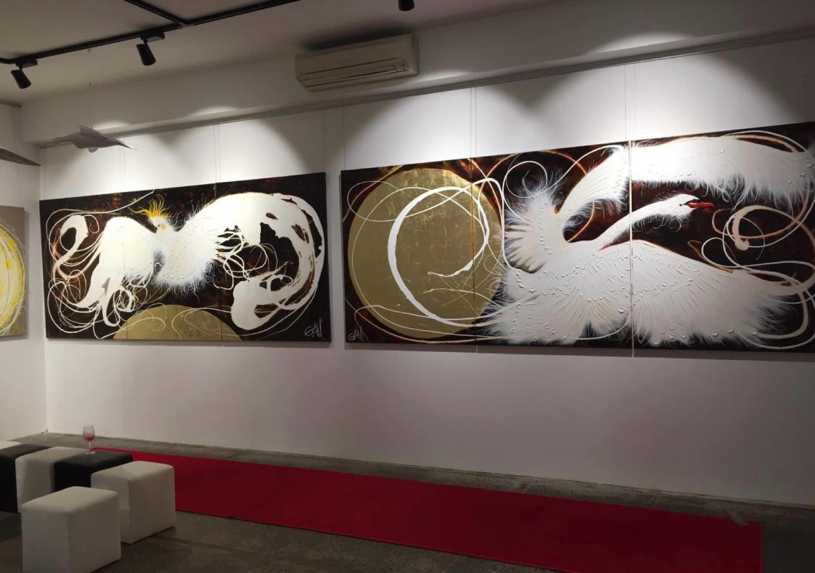 Two large multi panel bird artworks hung on a gallery wall from a rail system, lit by track lighting