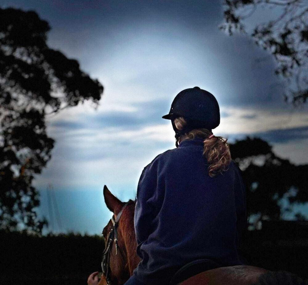A girl on horseback at dusk under an open sky